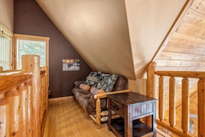 Une chambre à coucher confortable, aménagée en mezzanine, avec un plafond en pente, un plancher en bois, un canapé marron agrémenté de coussins à motifs et une petite table en bois.