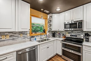 Une cuisine moderne avec des meubles blancs, des appareils en acier inoxydable, une fenêtre offrant une belle vue et un pare-feu décoré de carreaux gris et blancs.