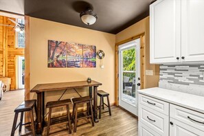 A kitchen with a wooden table and stools, a white cabinet, and a painting on the wall. - Peaceful 3BR w/Hot Tub*Fireplace*BBQ*Resort Pools (Gatlinburg)