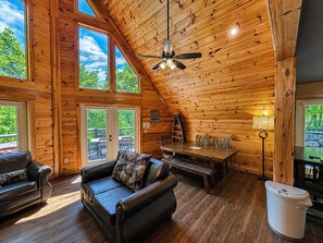 Eine geräumige Holzhütte mit Essbereich, einer Couch und einem Deckenventilator.