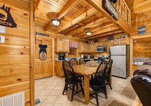Ein Holzblockhaus-Interieur mit Esstisch, Stühlen, Küchengeräten und einem Kamin.