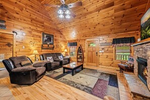 A cozy cabin interior with a fireplace, leather sofa, and a ceiling fan. - Pet Friendly 2BR w/Hot Tub*Firepit*Jacuzzi*Yard! (Sevierville)