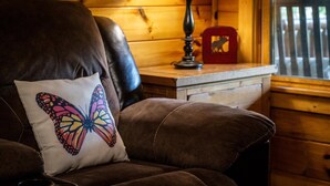 En brun lædersofa med en farverig sommerfugl-pude, et trænatbord med en lampe, og en rød dekorativ genstand.