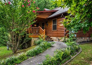 Eine Holzhütte mit Steinunterbau, einer Holzveranda und einem Steinweg, der zum Eingang führt.