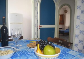 Ein Esstisch mit blauer Tischdecke, einer Weinflasche, Weingläsern und einer Obstschale.