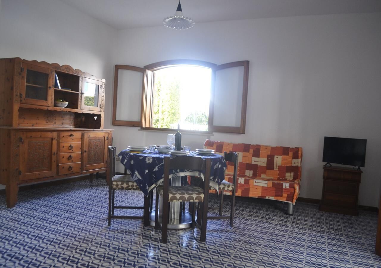 A dining area with a table set for four, a wooden cabinet, a patterned sofa, and a television on a stand.