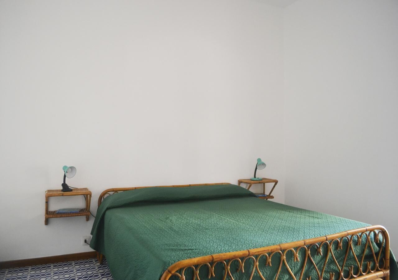 A single bed with a green bedspread, two bedside tables with lamps, and a patterned floor.