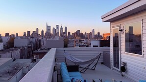 Een terras op het dak met uitzicht op de skyline van de stad, een hangmat en een blauwe bank.