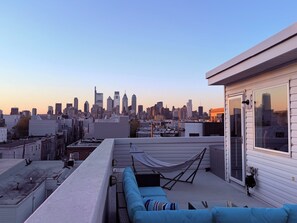 Eine Dachterrasse mit Blick auf die Stadtlandschaft, einer Hängematte und einem blauen Sofa.