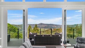 A modern interior with a large sliding glass door leading to an outdoor deck with a view of rolling hills and mountains. - Trinity Vista by Avantstay Private Dual-zone Spa + Fire Pit + Outdoor Dining + Views Sonoma Wine Country (Glen Ellen)