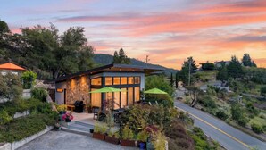 A modern house with a stone facade, large windows, and outdoor seating with umbrellas. - Trinity Vista by Avantstay Private Dual-zone Spa + Fire Pit + Outdoor Dining + Views Sonoma Wine Country (Glen Ellen)