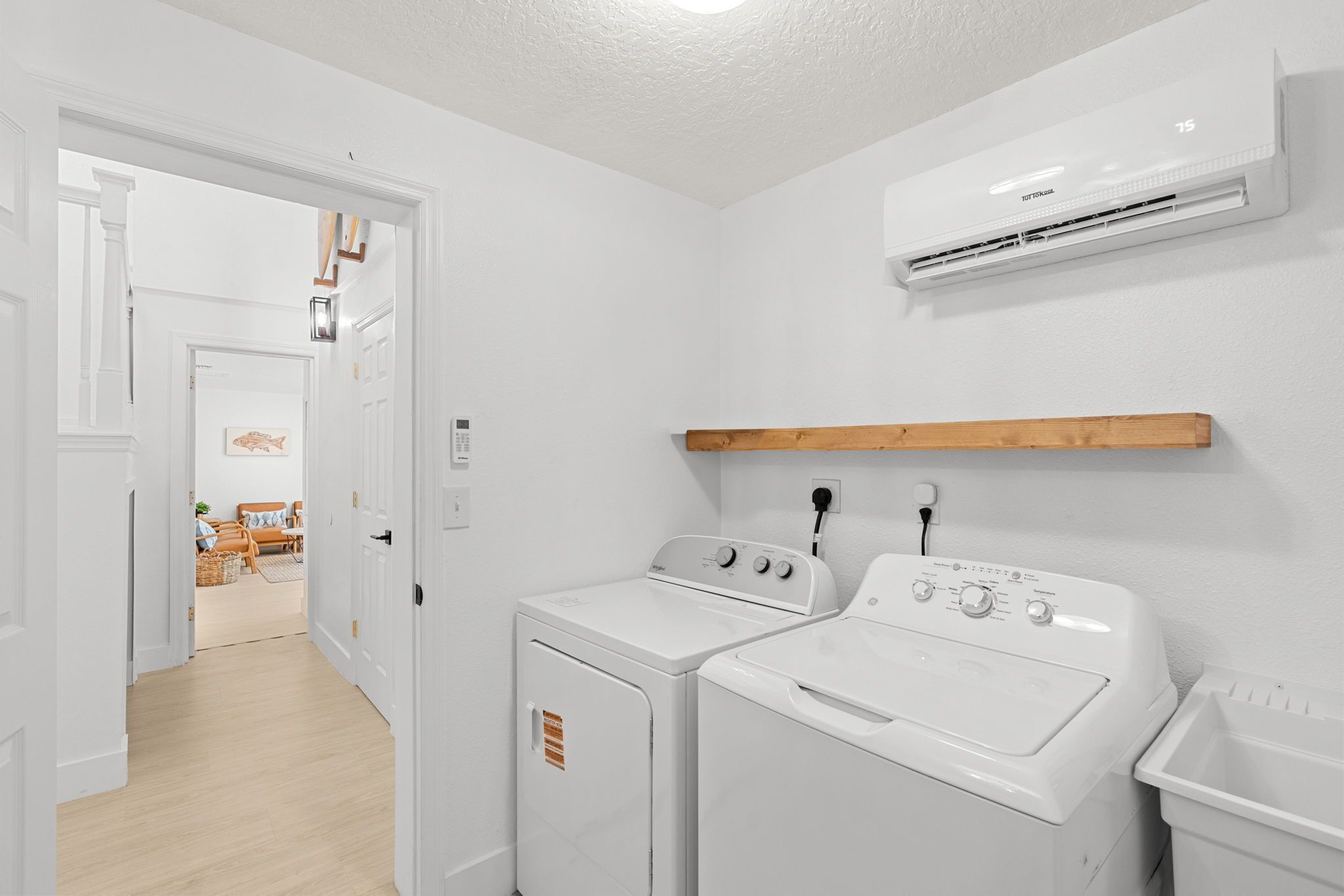 A laundry room with two white washing machines, a wooden shelf, and an air conditioning unit.