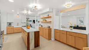 A modern kitchen with wooden cabinets, a marble island, and pendant lighting. - 504 Colony Street (Melbourne Beach)