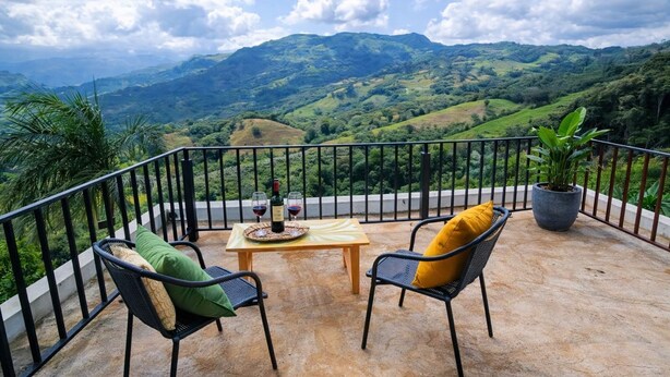 Ein Balkon mit Tisch, zwei Stühlen, einem Blumentopf und einer Weinflasche.