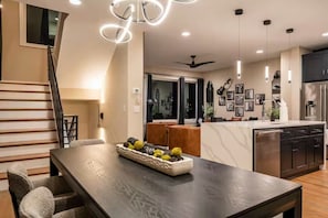 Una cocina moderna con una isla central, un comedor con mesa de madera oscura y una escalera que sube a un nivel superior.