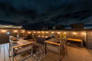 Terraza al aire libre con asientos, luces colgantes y vista al cielo.