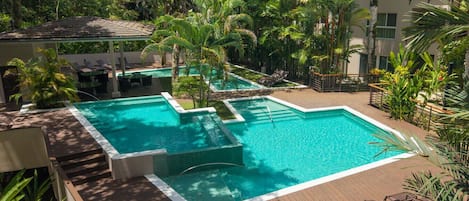 En pool på taket med ett trädäck, omgiven av frodig grönska och palmer.
