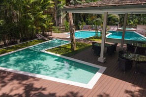 Zona de piscina amb diverses piscines, gandules i una zona de seients coberta.