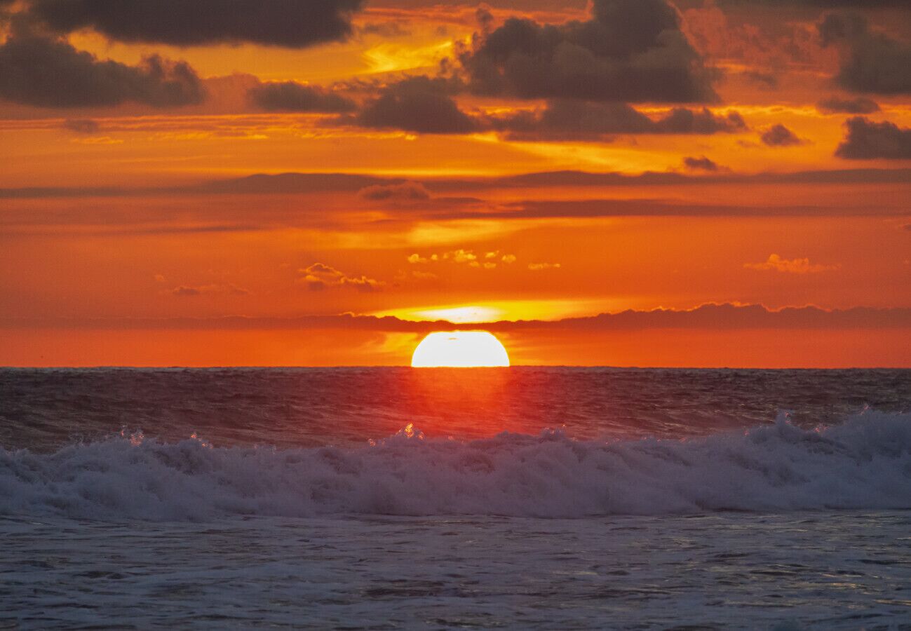 Un coucher de soleil sur l’océan, avec des vagues au premier plan.