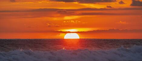 Un coucher de soleil sur l’océan, avec des vagues au premier plan.