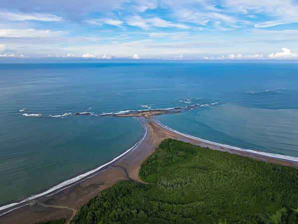 Vista aèria d'una zona costanera amb una platja, una carretera i una àrea forestal.