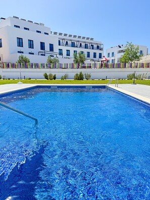 Ein Swimmingpool mit Metallleiter, umgeben von einem weißen Gebäude mit Balkonen und einem bunten Zaun.