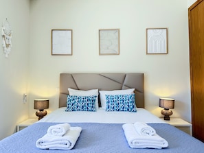 Ein Hotelzimmer mit einem Bett, zwei Kissen, zwei Nachttischlampen und drei gerahmten Kunstwerken an der Wand.
