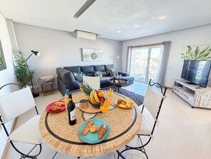 Ein modernes Wohnzimmer mit Essbereich, einer Couch, einem Fernseher und einem Balkon mit Blick.