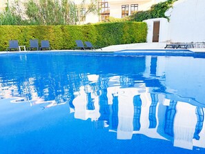 Ein Schwimmbecken mit klarem, blauem Wasser, umgeben von Liegestühlen und einer ordentlich geschnittenen Hecke.