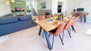 Ein modernes Wohnzimmer mit einer Couch, einem Esstisch mit Stühlen, einem Fernseher und einer Treppe, die in eine obere Etage führt.