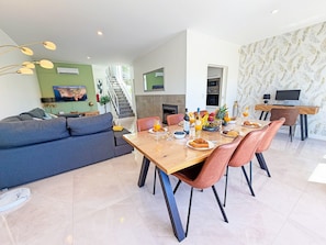 A modern living room with a sofa, dining table with chairs, a TV, and a staircase leading to an upper level. - Terras Novas Village Paradise By BeCherish (Albufeira)