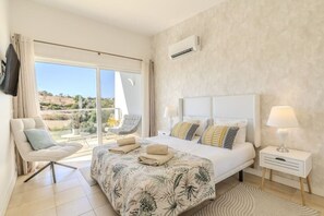 A bedroom with a bed, a chair, a nightstand, and a view through a large window. - Terras Novas Village Paradise By BeCherish (Albufeira)