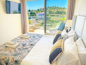A hotel room with a bed, a sofa, a TV, and a view of a hillside. - Terras Novas Village Paradise By BeCherish (Albufeira)