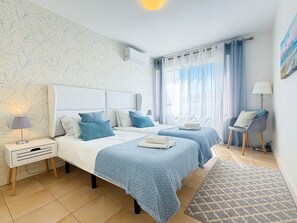 A hotel room with two beds, a nightstand, a lamp, a chair, and a view of the outdoors. - Terras Novas Village Paradise By BeCherish (Albufeira)