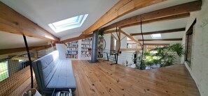 An attic room with wooden beams, skylights, a bookshelf, and a view of the outside.