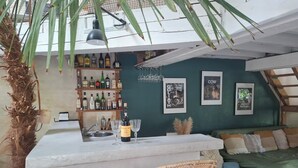 Een bar met een toonbank, twee rieten stoelen, een bank en een muur met ingelijste foto's.