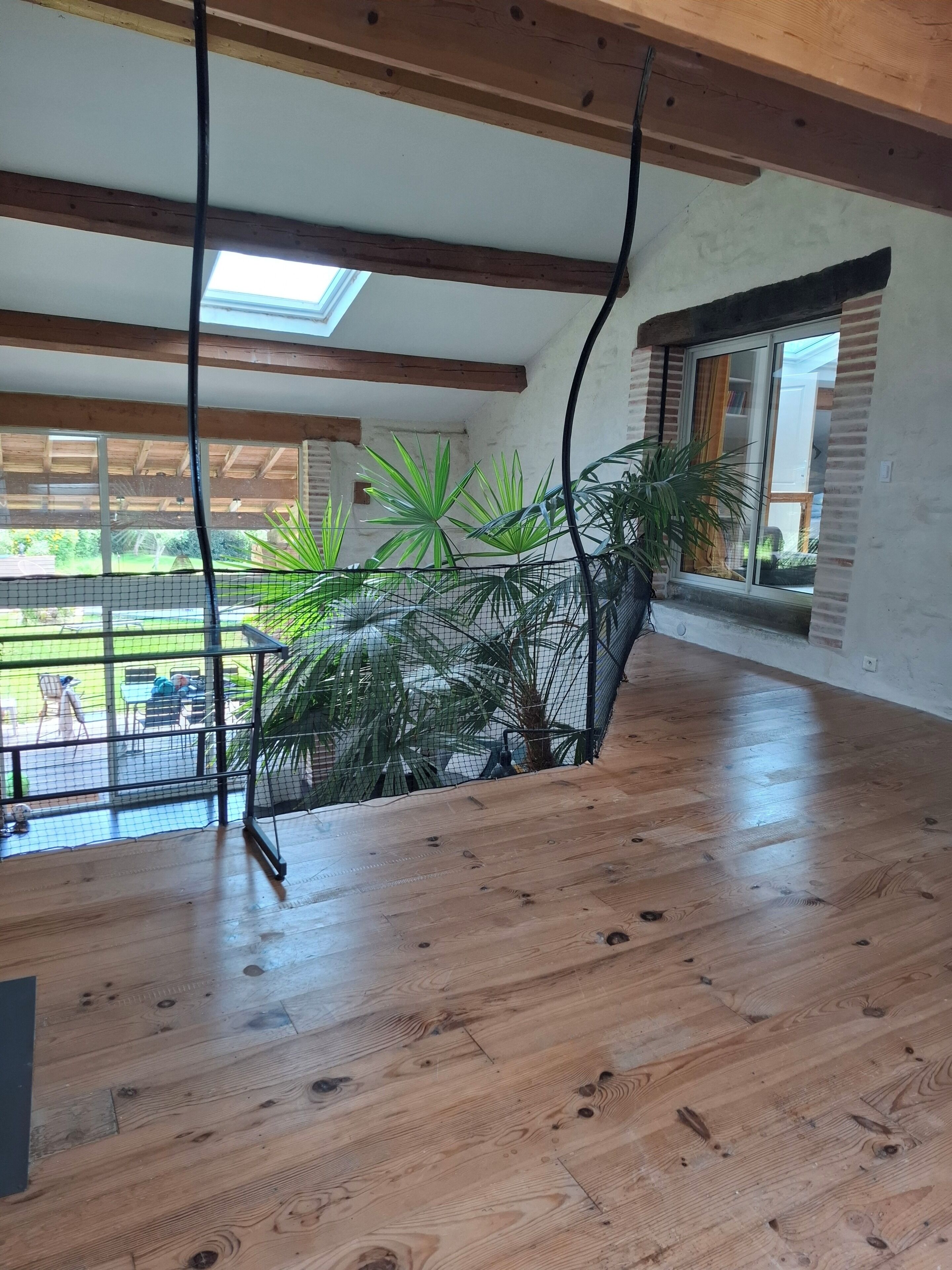 Een ruime kamer met houten vloeren, een groot raam met uitzicht op de omgeving en een plafond met zichtbare balken.
