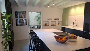 Een moderne keuken met een groot eiland, barkrukken, een spoelbak en uitzicht op de woonkamer.