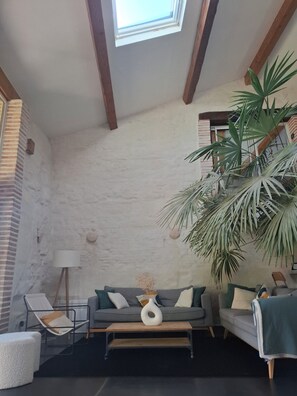 Una habitació amb un lucern, un sofà amb coixins, una taula de cafè, una cadira i una planta en test.