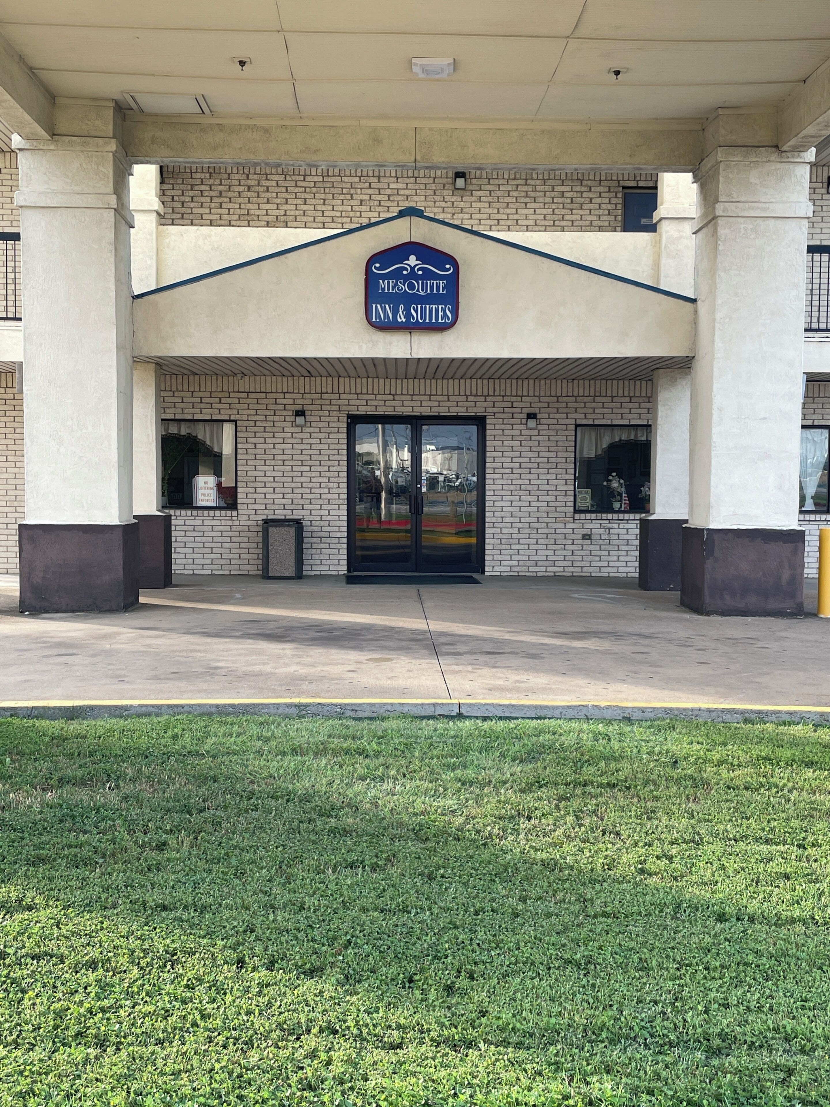 L’entrée d’un hôtel, avec une enseigne indiquant « Mesquite Inn & Suites », une façade en briques et une pelouse devant.