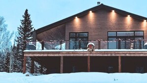 Une cabane en bois dotée d’une terrasse couverte, de grandes fenêtres et surplombant un paysage enneigé.
