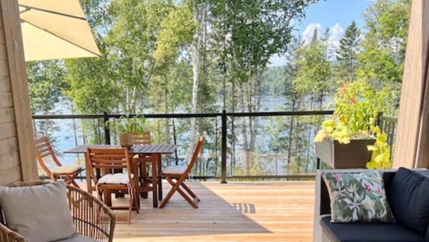 Une terrasse en bois, aménagée avec du mobilier d’extérieur, notamment un canapé, des fauteuils et une table, et offrant une vue sur une étendue d’eau.