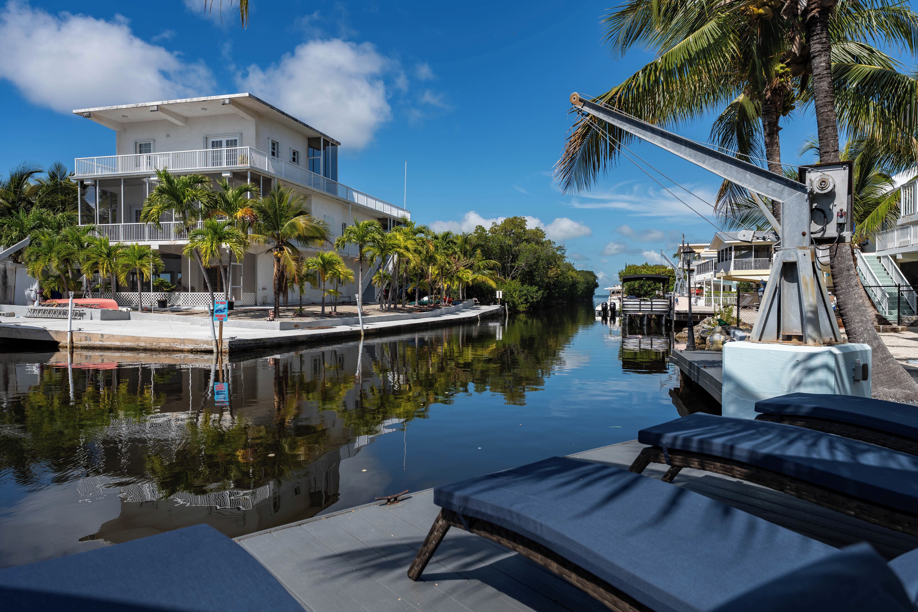A waterfront hotel with a pool, lounge chairs, and palm trees.