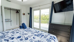 Une chambre avec un lit, une commode, une télévision et un balcon offrant une vue.