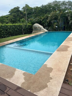 Una piscina rectangular amb aigua cristal·lina blava, envoltada d'un sòl de formigó i vegetació exuberanta.
