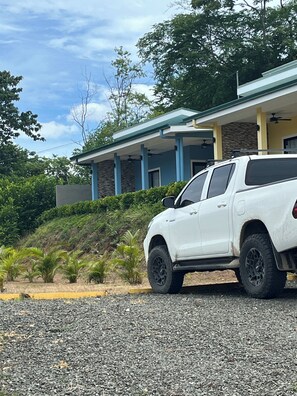 Un cotxe SUV blanc estacionat davant d'un edifici amb façana de pedra, columnes blaves i teulada inclinada.