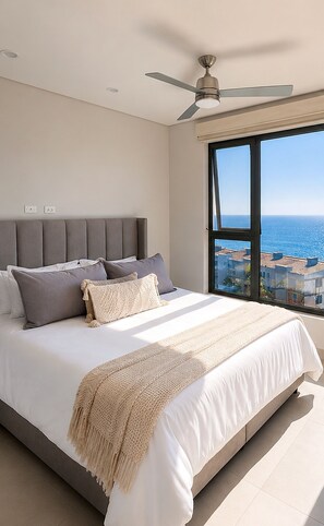 Een slaapkamer met een groot bed, een plafondventilator en uitzicht op zee.