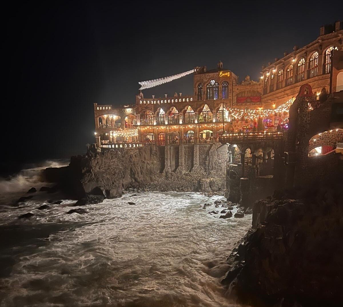 A historic building with arched windows and a balcony overlooking a rocky coastline.