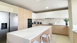 A modern kitchen with a marble island, stainless steel appliances, and wooden cabinetry. - Penthouse Pacific Luxury King 6BR/5BA Larcomar (Miraflores)