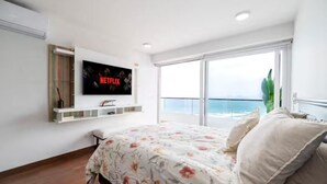 A bedroom with a bed, a TV mounted on the wall, a balcony with a view, and a plant. - Penthouse Pacific Luxury King 6BR/5BA Larcomar (Miraflores)